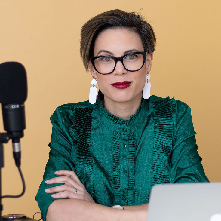 Ana Xavier, The Podcast Space in green top, sitting next to mic and laptop on yellow background